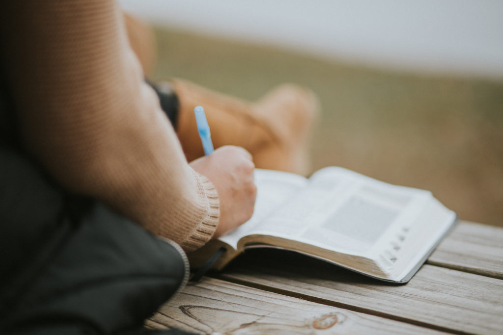 Person writing in Bible on a bench.Information on BCA Adult Ministries below.