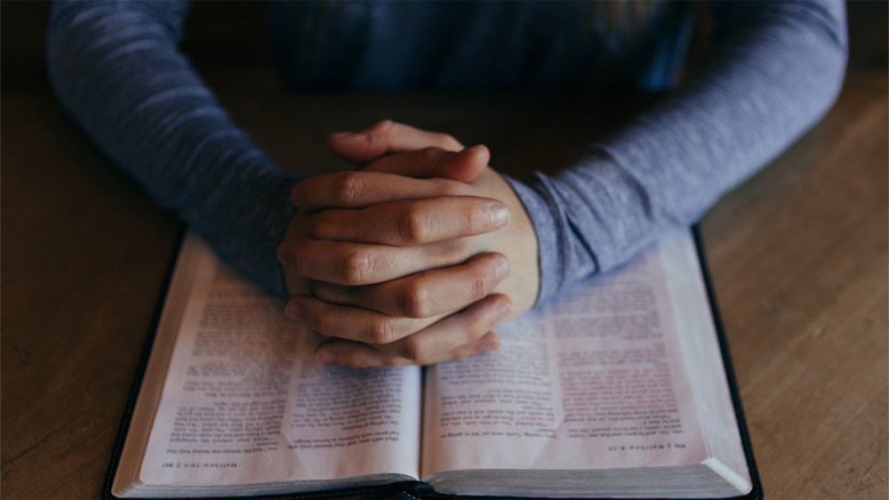 Praying hands over open Bible