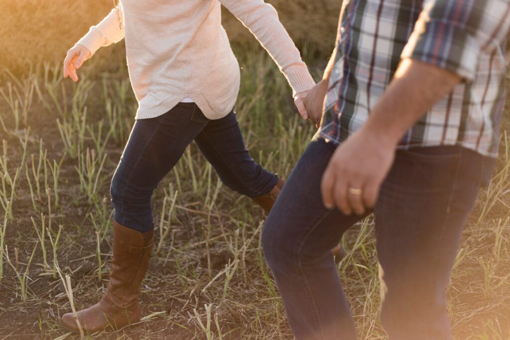 A couple holding hands and walking through a field