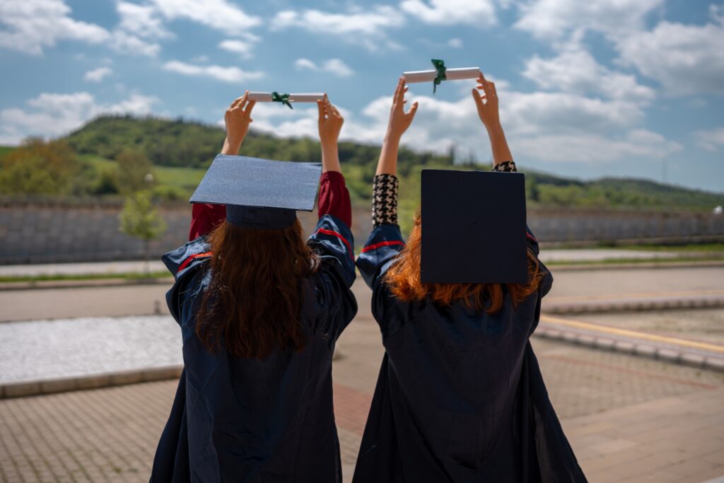 Two women holding their degrees up to the sky